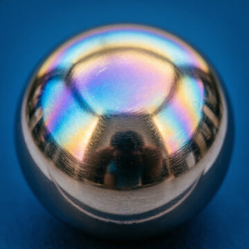 Anodized titanium macro with iridescent oxide layer on solid deep blue background