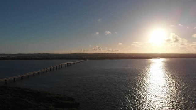 Smooth drone aerial view panning over Kurima Bridge into bright golden sunset glare, Miyakojima, Okinawa