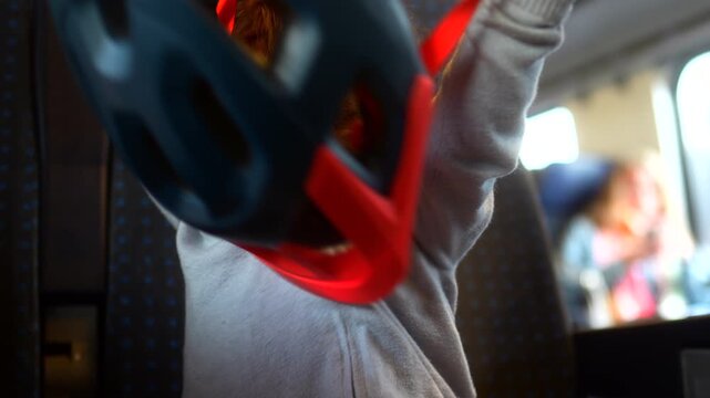 Toddler trying to put on bicycle helmet while riding passenger train, playful childhood travel moment highlighting curiosity, learning, independence and everyday family adventure