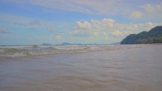 Peaceful seascape footage from water level, small ocean waves on a beautiful sandy beach with mountains and forest in the background.