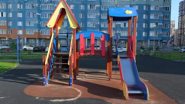 Child playing on colorful playground equipment near apartment building. Kid climbing and sliding structure in residential courtyard. Active childhood leisure time.