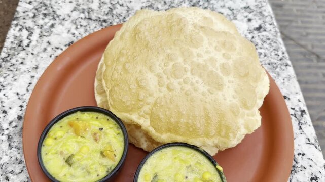 Slow push-in 4K footage of golden puffed puri served with creamy Indian vegetable curry in small bowls on a red plate, showcasing a traditional breakfast with rich texture and vibrant colors.