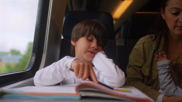 Young boy completing homeschool lessons while traveling by train with mother nearby, authentic family learning scene highlighting education on the go, concentration, literacy and flexible learning