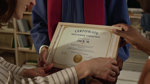 Cropped shot of teenager holding high school completion certificate while diverse parents touch wooden frame in celebration. Clip is ideal for academic success and graduation marketing