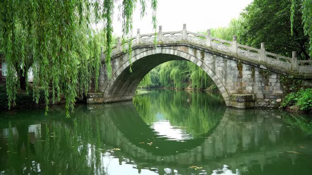 The natural scenery of the stone arch bridge in the Jiangnan water town, with the stone bridge reflecting the willows