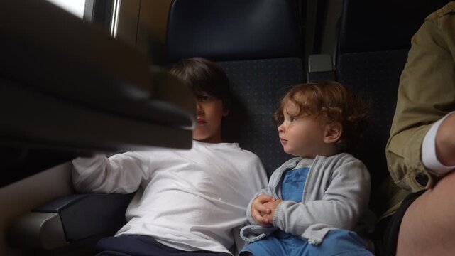 Toddler grabbing object beside older brother during passenger train journey, authentic sibling interaction highlighting curiosity, sharing, gentle boundaries and everyday family travel