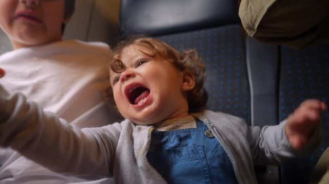 Excited toddler holding fresh nectarine while riding passenger train beside older sibling, joyful family travel moment highlighting healthy snacking, curiosity and childhood adventure