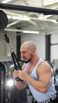 Muscular athlete performs cable triceps pushdown with a rope attachment during an upper body strength workout in a modern fitness gym. Healthy lifestyle and functional training.