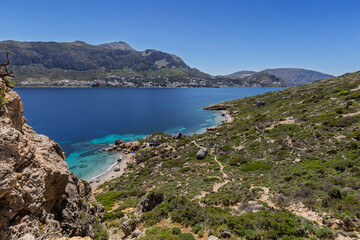Fototapeta premium Rugged and lush landscape, beaches, coastline and the Aegean Sea on Telendos island in Greece on a sunny day. Mountainous Kalymnos island is in the background.