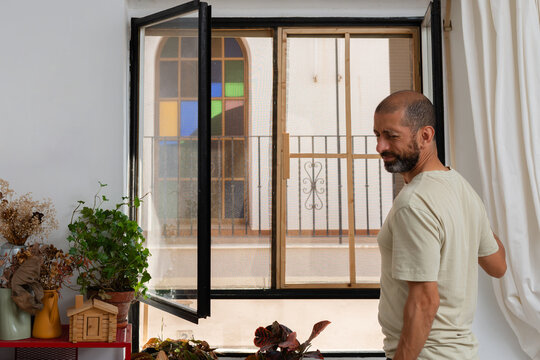 Man opening window and reacting to hot air during summer heatwave at home