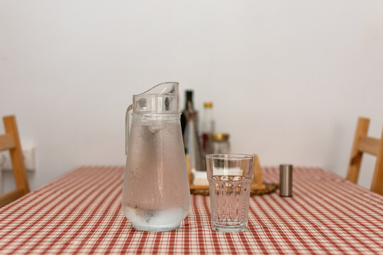 Cold glass water pitcher with condensation and drinking glass on table