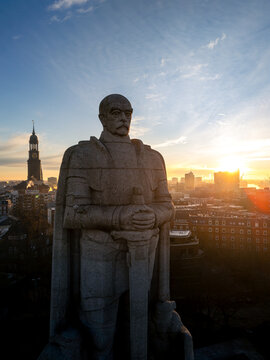 Aerial view of the Bismarck Monument with the city skyline and St. Michael's Church visible under the golden sunset light in Hamburg, Hamburg, Germany.