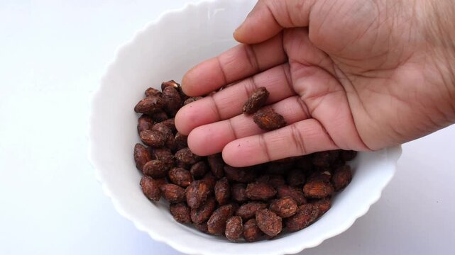 hand picking jaggery cocoa coated almonds from a white bowl, highlighting a delicious and healthy alternative to sugary snacks