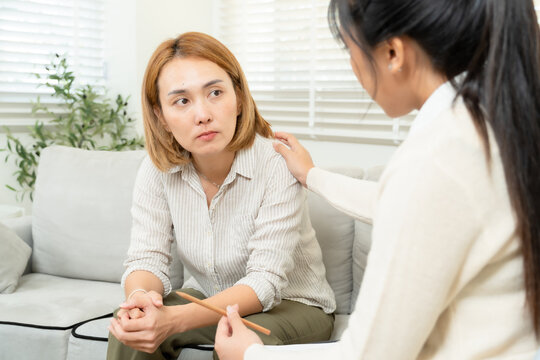 Female asian psychologist comforting concerned single mother during counseling session in therapy room offering mental health support for parenting ADHD child in safe emotional environment