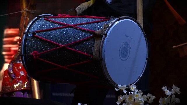 musician's hands playing a large traditional dhol drum under colorful stage lights at night