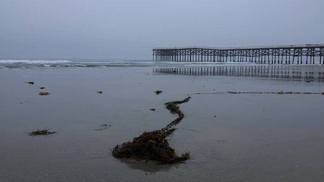 Crystal pier and Pacific beach on early gloomy summer morning under overcast sky with wave coming onshore, San Diego, Southern California 