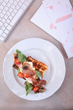 Viennese waffles with bacon, champignons and cherry tomatoes on potato pillow. Classic waffles with bacon. Computer keyboard. Concept of business breakfast. Top view