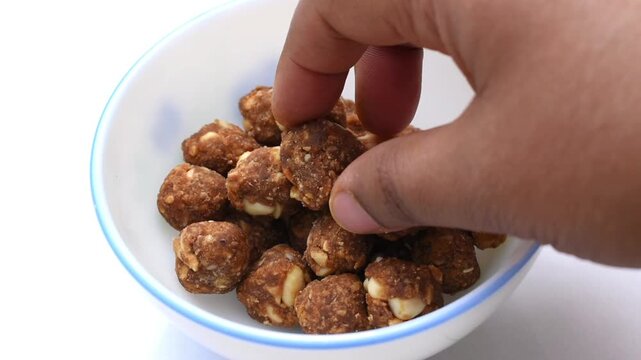 hand picking a homemade jaggery and mixed nut ball from a white bowl, highlighting a nutritious no-refined-sugar snack.