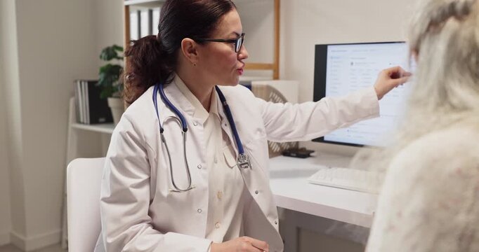 Doctor and senior patient consultation in clinic. Healthcare expert gives advice and diagnosis about medicine, reviewing records on a computer in the office. Concept of supportive senior care.