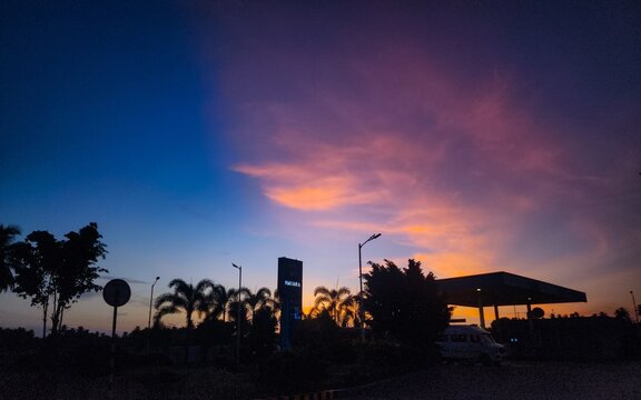 Theni, Tamil Nadu, India &ndash; June 27, 2026: Evening silhouette of a Nayara Energy petrol station with a parked van beneath glowing sunset clouds in Theni district, Tamil Nadu