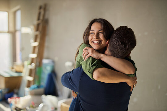 Happy young couple embracing on a residential construction site, celebrating their new apartment renovation.