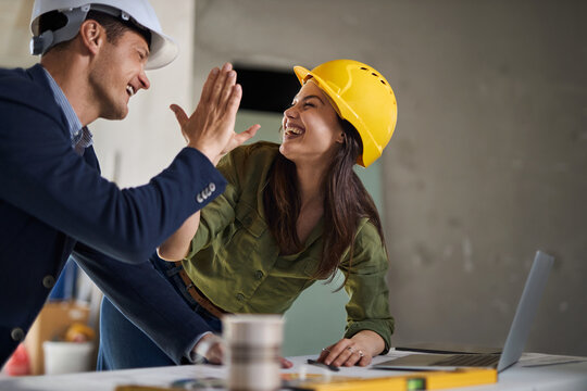 Young interior designers using laptop at construction site and giving each other high-five.