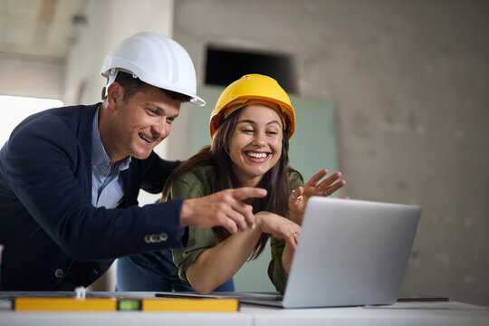 Happy interior designers cooperating while working on laptop at construction site.