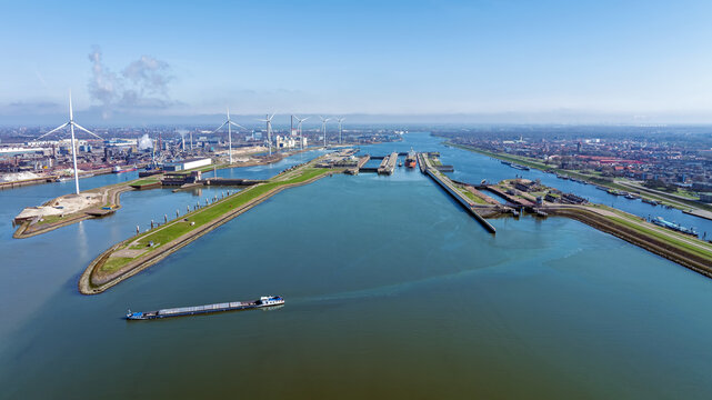 Aerial view of the IJmuiden sea locks with a cargo ship navigating the canal, surrounded by wind turbines and industrial infrastructure in IJmuiden, North Holland, Netherlands.