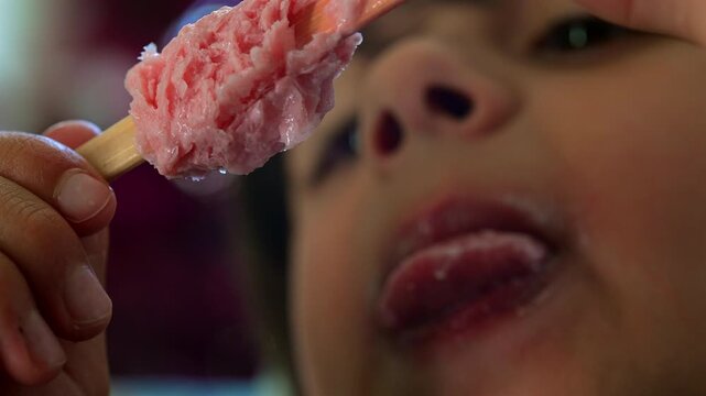 Child taking bite of strawberry ice cream bar in close-up, celebrating summer treats, everyday happiness and carefree childhood