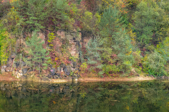 Autumn forest reflection on lake water surface with rocky cliffside cliff landscape and peaceful mood