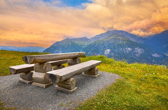 Grossglockner panoramic view in Austrian Alps. Wooden table with bench for hikers in Austria.  picturesque view at snowbound mountains and green knolls with forests. 