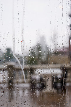 Raindrops trickle down the glass,Water Droplets on a pane of glass with blurred city background,View from a window showing rain falling rainy day,Copy space.