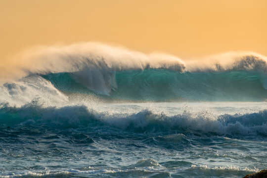 Aerial view of a powerful turquoise ocean wave crashing with sea spray under warm golden hour light Torndirrup, Western Australia, Australia.