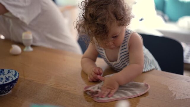 Toddler wiping spilled water from kitchen table, highlighting responsibility, early learning and everyday family life