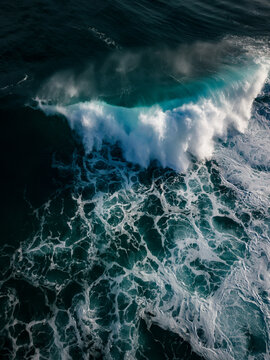 Aerial view of a powerful turquoise wave breaking into white sea foam against the dark ocean depths near Blowholes Road in Torndirrup, Western Australia, Australia.