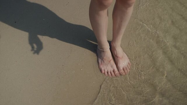 Woman's feet soaking in clear ocean water on a sandy beach