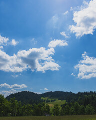 Obraz premium Sunny mountain valley beneath dramatic blue sky and towering summer clouds