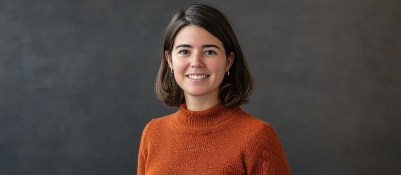 A woman wearing an orange turtleneck smiles in front of a dark gray background.