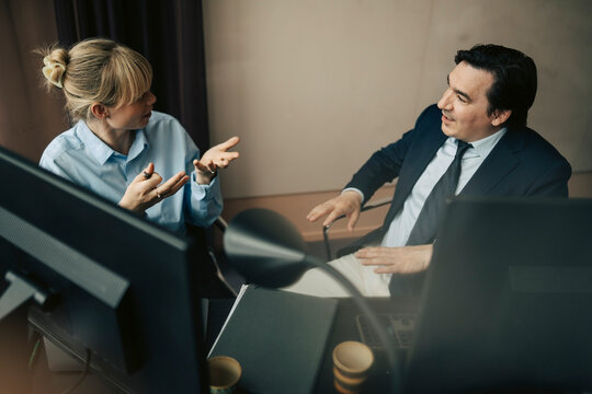 High angle view of male and female business professionals talking with each other at desk in office