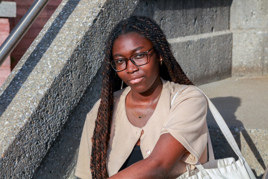 Confident young Black university student with glasses and a tote bag sitting on campus stairs