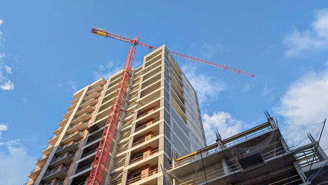 Building with a large red crane on a construction site, workers developing a new high rise residential or commercial complex, signifying progress and urban expansion