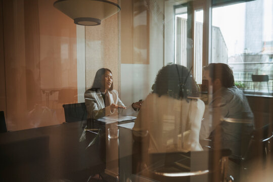 Female financial advisor explaining agreement deed to business partners in office meeting seen from glass wall