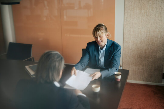 Smiling businesswoman showing agreement documents to her coworker in corporate room