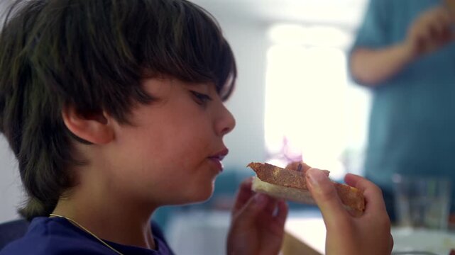 Young boy eating bread during family meal at home, highlighting healthy eating, family routines and everyday childhood