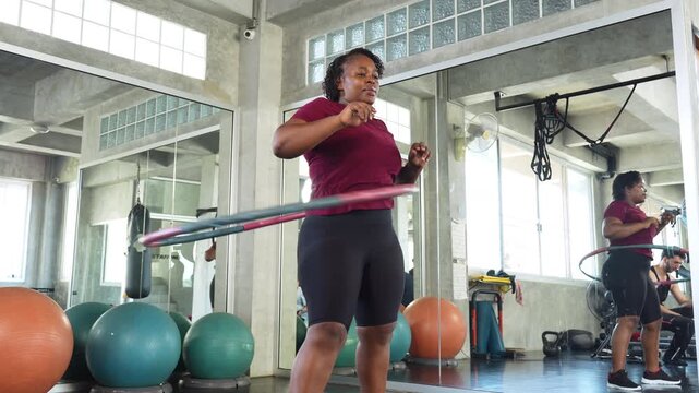 African woman exercising with a hula hoop in a modern gym, improving fitness, balance and weight loss through cardio training and an active healthy lifestyle.