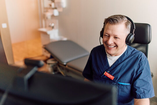 Happy male doctor communicating with patient through video call while sitting in room at hospital