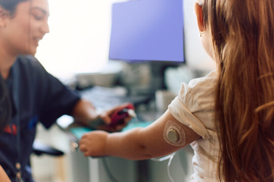 Girl with long hair wearing glucose tracking device on her arm during her visit at hospital