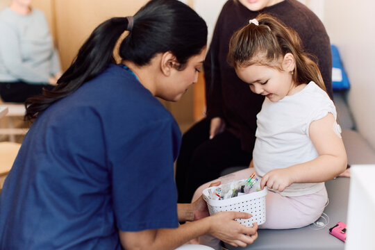 Female doctor holding out basket of small toys for girl after her checkup