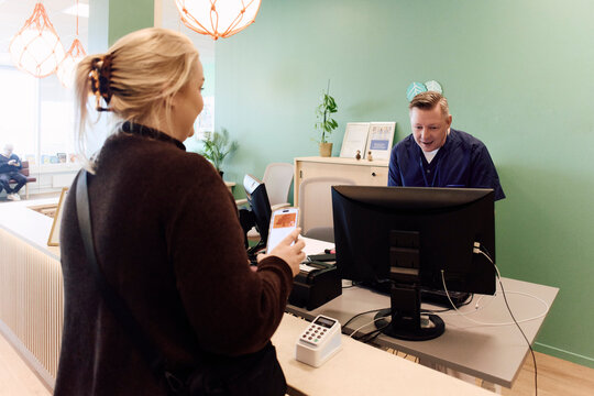 Male receptionist assisting female patient at modern medical clinic counter
