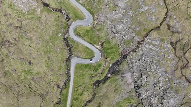Drone shot of vehicle driving on serpentine switchback road in Faroe Islands